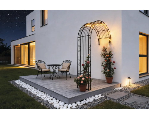 Terrass med rosenbåge, bordsgrupp och dekoration i trädgården