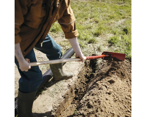 En person gräver ett dike i trädgården med en spade.