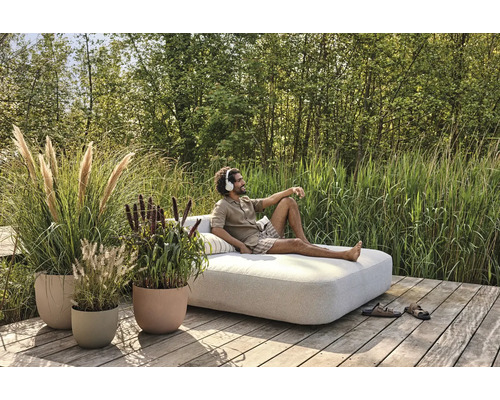 Man kopplar av med hörlurar i en loungesoffa i trädgården, omgiven av planteringskärl med prydnadsgräs.