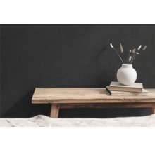 Dekorativ scen med träbänk, böcker och vas med torkade blommor framför en mörk vägg