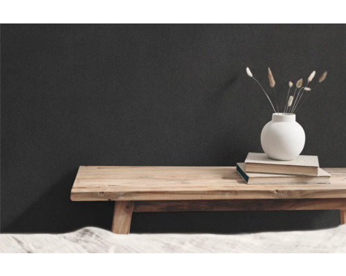 Dekorativ scen med träbänk, böcker och vas med torkade blommor framför en mörk vägg