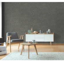 Vardagsrum med fåtölj, sidobord och byrå framför en strukturerad väggtapet.