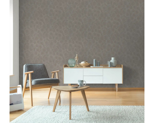 Vardagsrum med grå mönstrad tapet, fåtölj, sidobord och byrå.