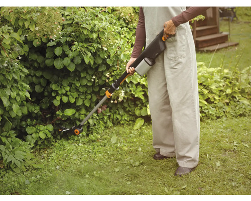 Person använder batteridriven grässax för trädgårdsarbete