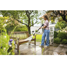 En kvinna rengör en träbänk med en högtryckstvätt i trädgården.