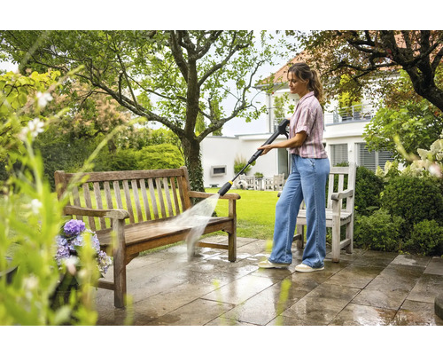 En kvinna rengör en träbänk med en högtryckstvätt i trädgården.