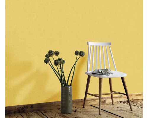 Dekorativ vägg med gul tapet, en blombukett i en vas och en stol.