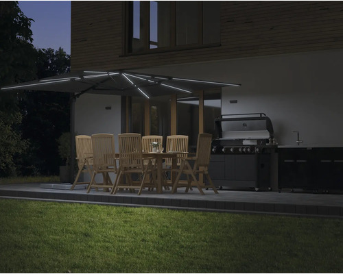 Upplyst trädgårdssittplats med parasoll, bord, stolar och grill