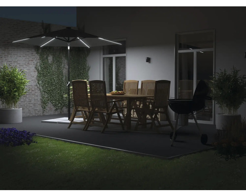 Belyst trädgårdsparasoll ovanför en sittgrupp i trä och en grill på en terrass