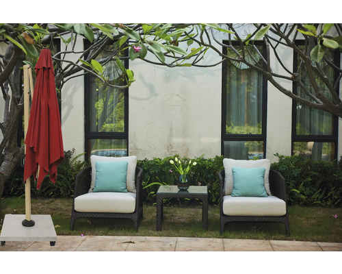 Trädgårdsscen med stängt parasoll, två fåtöljer med kuddar och ett sidobord med en blomvas.