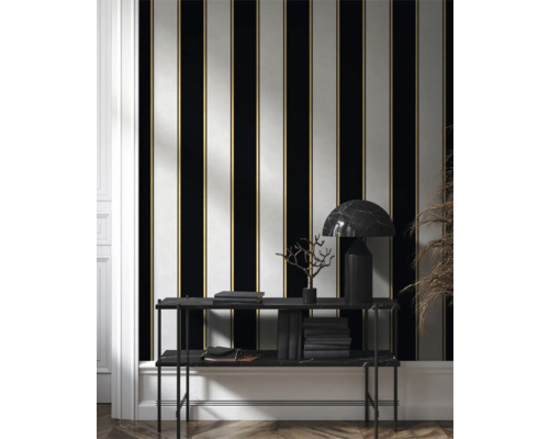 Rumsöversikt med randig tapet i svart, vitt och guld samt hylla med böcker och lampa.