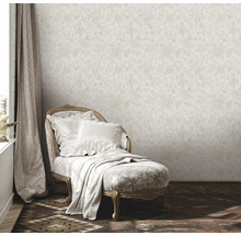 Miljöbild med beige blommig tapet, schäslong med kuddar och filt samt gardin