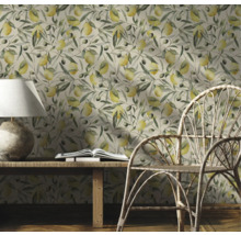 Dekorativt rum med en tapet med citroner och olivkvistar, ett träbord, en lampa, en bok och en rottingstol.