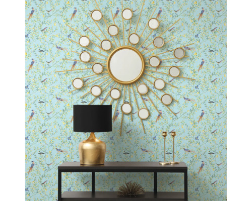 Dekorativ interiör med en rund spegel i form av en sol, en bordslampa och en konsol mot en mönstrad tapet.