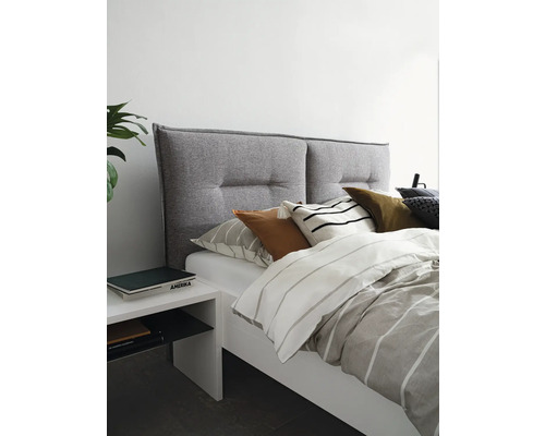 Säng med grå tygklädd sänggavel och vitt sängbord