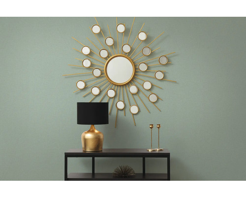 Dekorativ inredning med spegel i form av en sol, lampa och ljusstakar på en hylla.