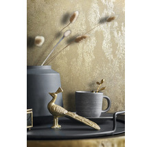 Dekorativ stillebenbild med guldfärgad tapet, vas, kopp och påfågelfigur