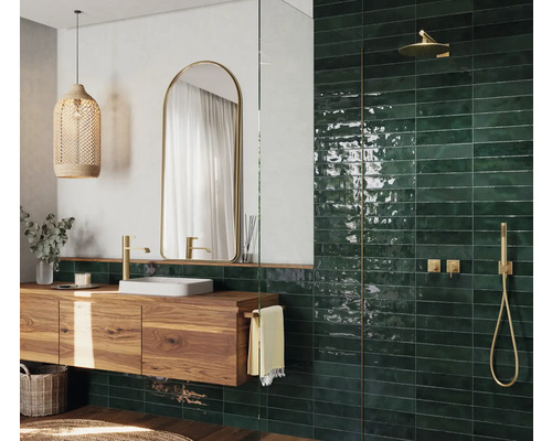 Modernt badrum med tvättställ i trä, spegel, hängande lampa och gröna kakelplattor i duschen