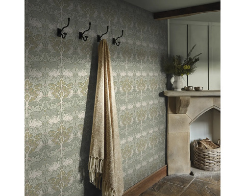 Detaljbild av ett rum med mönstrad tapet, hatthylla, filt och öppen spis