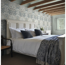 Sovrum med mönstrade tapeter, säng och exponerade takbjälkar.