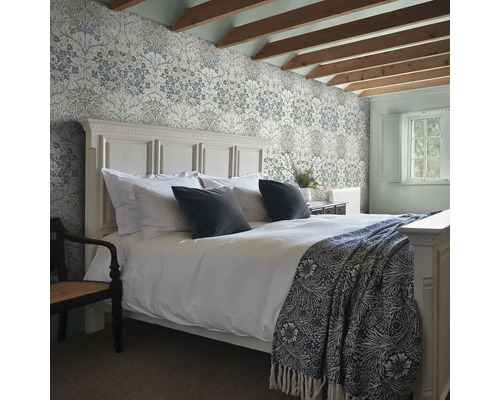 Sovrum med mönstrade tapeter, säng och exponerade takbjälkar.