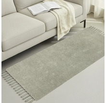 Grå gångmatta med fransar bredvid en soffa med bok