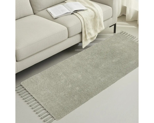 Grå gångmatta med fransar bredvid en soffa med bok