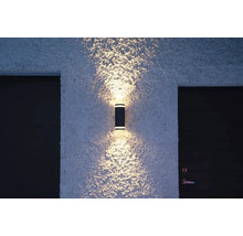 En cylindrisk vägglampa belyser en fasad.