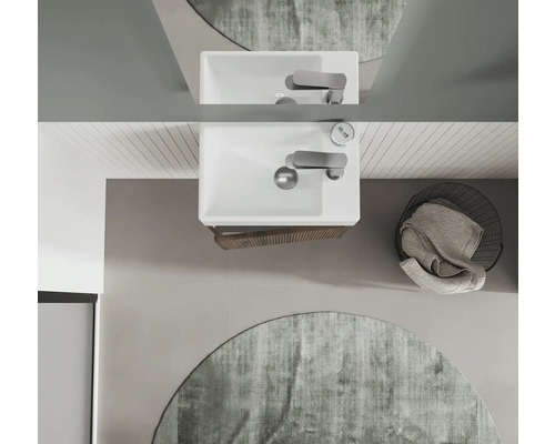 Översikt av ett badrum med handfat, blandare, spegel, rund matta och tvättkorg