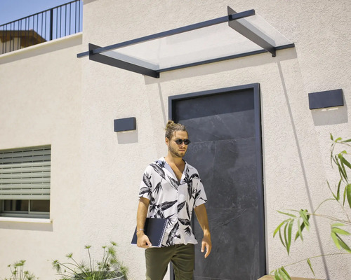 Modernt entrétak med svart metallram och transparent panel över en mörk ingång på en ljus husfasad.