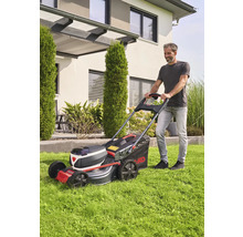 Man klipper gräs med en AL-KO batteridriven gräsklippare framför ett hus.