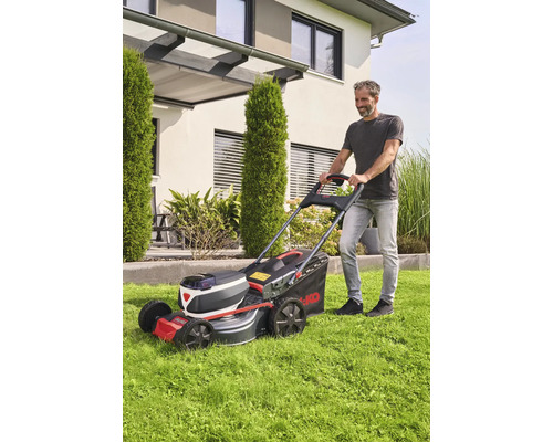 Man klipper gräs med en AL-KO batteridriven gräsklippare framför ett hus.