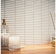 Scen med vita, avlånga väggplattor, tvålpump, ljus och handduk på ett träbord