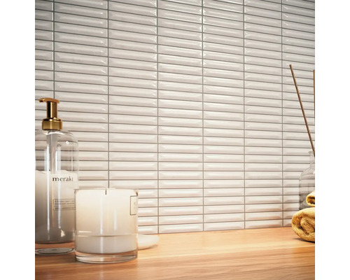 Scen med vita, avlånga väggplattor, tvålpump, ljus och handduk på ett träbord