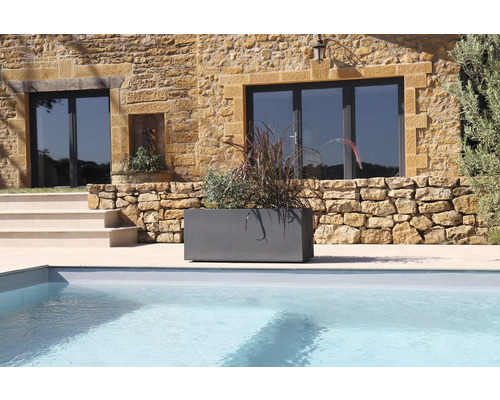 Grå planteringslåda med växter bredvid en pool framför ett hus