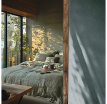 Sovrum med säng, kuddar, täcke och växter bredvid ett fönster