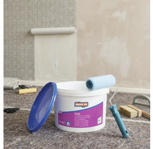 Miljöbild med en hink non-woven tapetklister, en färgroller, en tapetborste och en påbörjad tapet på väggen