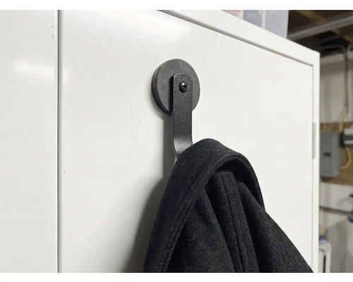 Svart magnetisk klädkrok på en vit yta med en jacka hängande på den