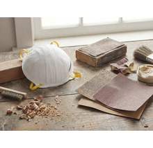 Dammskyddsmask, sandpapper och verktyg på en arbetsbänk