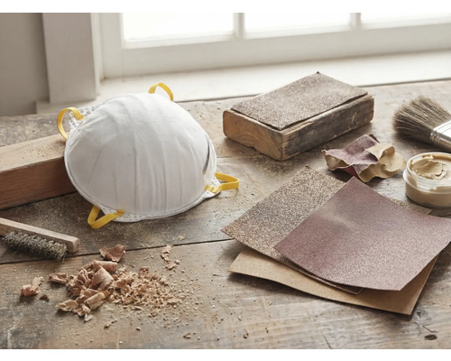 Dammskyddsmask, sandpapper och verktyg på en arbetsbänk