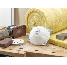 Scen med dammmask, sandpapper, slipmaskin och isoleringsull på en arbetsbänk.