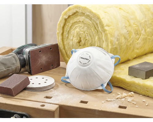 Scen med dammmask, sandpapper, slipmaskin och isoleringsull på en arbetsbänk.