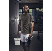 Hantverkare med t-shirt, shorts, hink och murslev på en byggarbetsplats.