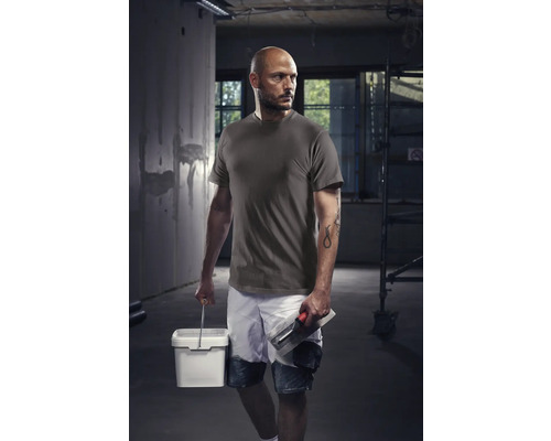 Hantverkare med t-shirt, shorts, hink och murslev på en byggarbetsplats.