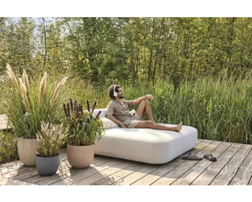 Utomhusscen med en man på en dagsbädd, omgiven av växter i planteringskärl