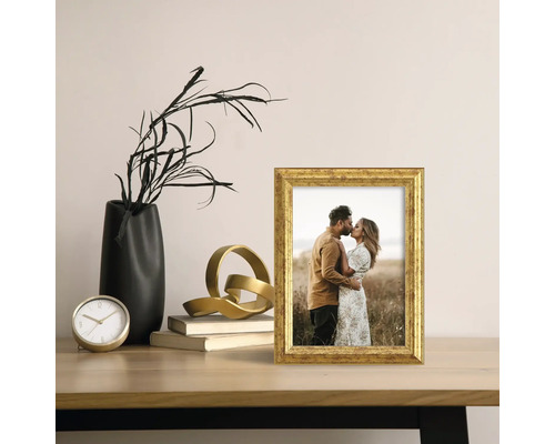 Dekorativ scen med en gyllene fotoram, en svart vas och en gyllene skulptur