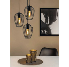 Tre svarta hänglampor med lampskärmar i tråd över ett matbord med dekoration