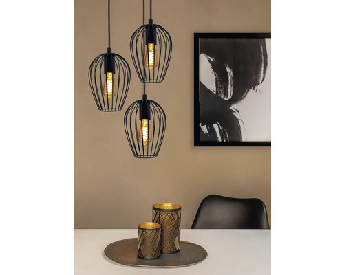 Tre svarta hänglampor med lampskärmar i tråd över ett matbord med dekoration