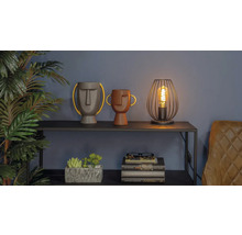 Dekorativ scen med två vaser med ansikten, en lampa och en stapel böcker på en hylla.