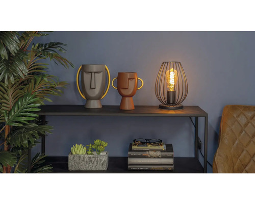 Dekorativ scen med två vaser med ansikten, en lampa och en stapel böcker på en hylla.